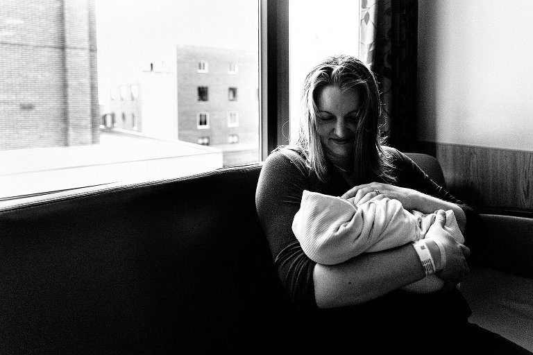 Mom smiles at newborn baby in urban hospital room