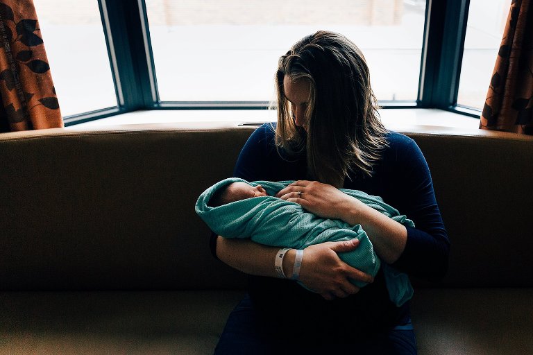 mom holds newborn on hospital couch on cloudy day