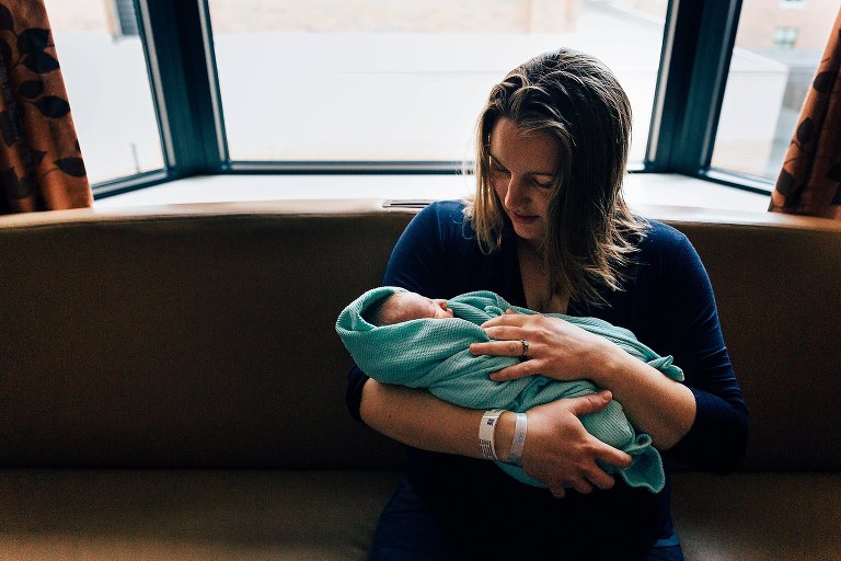 mom holds newborn baby on hospital room couch 