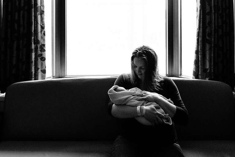 Mom holds newborn baby on hospital room couch 