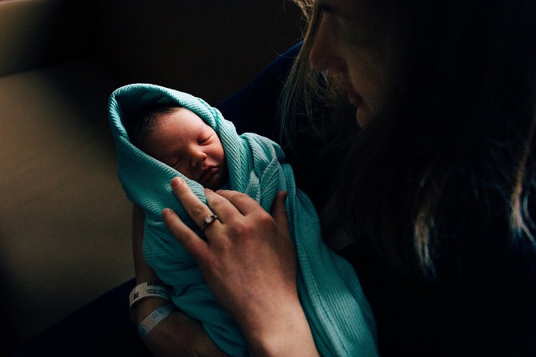 New mom holds newborn baby. Hospital blanket, hospital bracelets. 