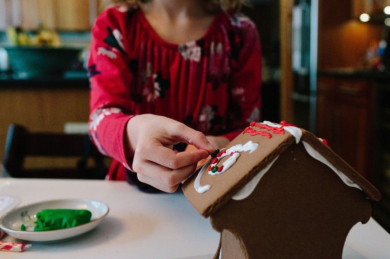 Girl attaches candy to gingerbread house