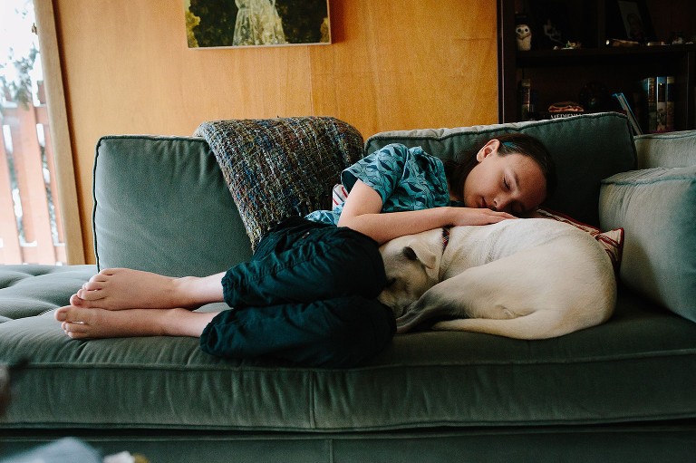 Boy sleeps with curled up dog on the couch in front of fire