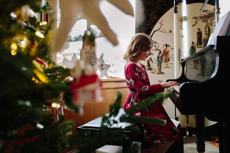 Girl plays piano, Christmas tree in foreground 