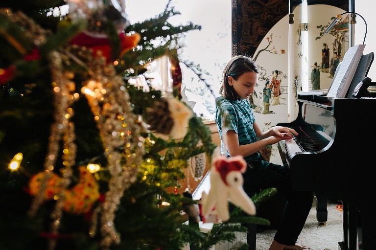 Boy plays piano, Christmas tree in foreground 