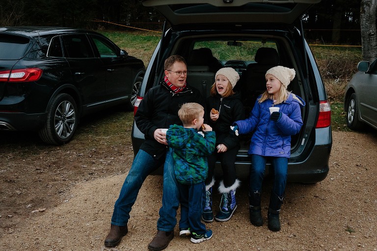 Family sits in the back of the van, talking to each other and eating donuts and drinking cider