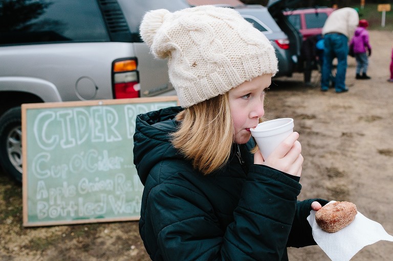 Girls drinks hot cider and holds donut. 