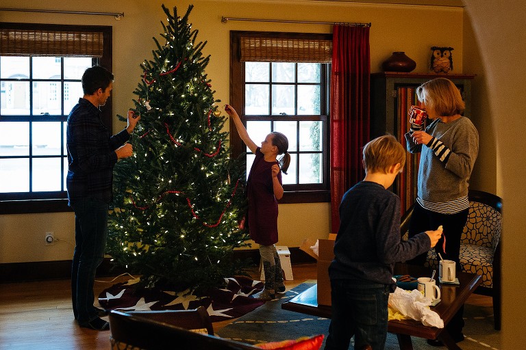 Family decorates Christmas tree in living room, mom drinks hot chocolate