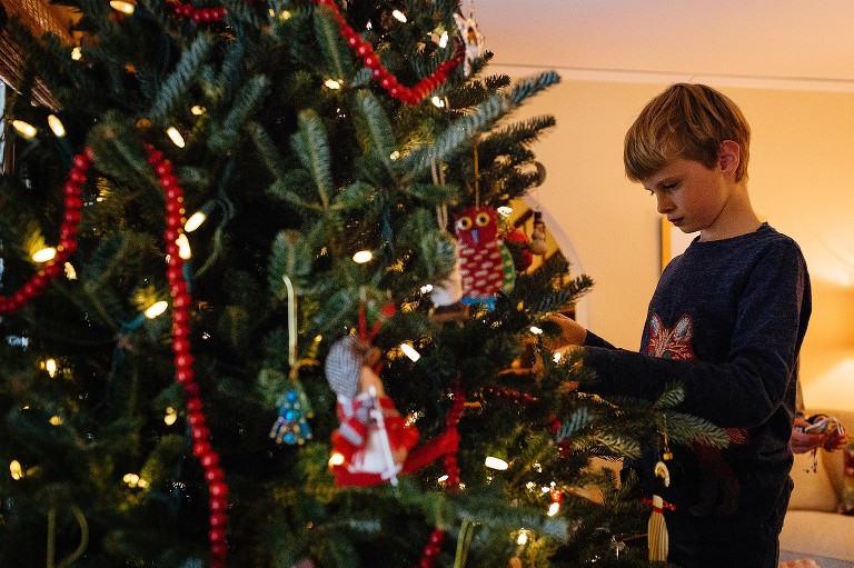 Boy decorates Christmas tree in living room