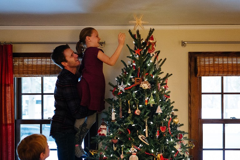 Dad and daughter place star on Christmas tree in living room