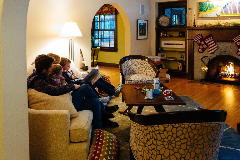 Family reads Christmas story on the couch. Stockings hung over fire in fire place 