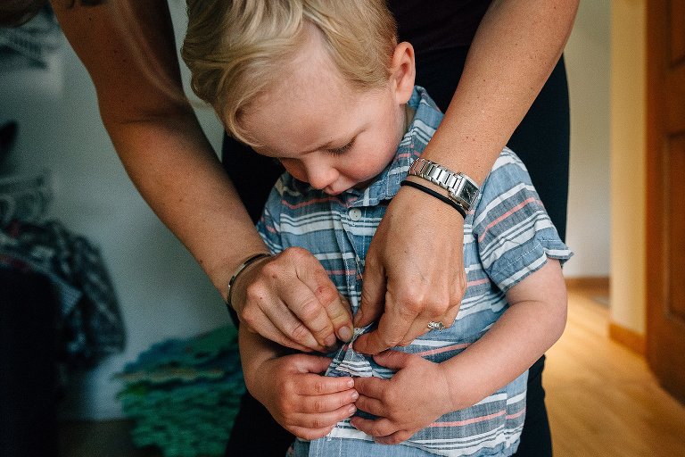 Mom helps preschooler button his shirt