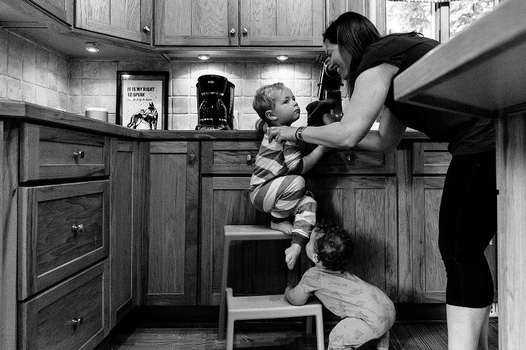 Mom washes preschooler's face while toddler climbs up step stool 