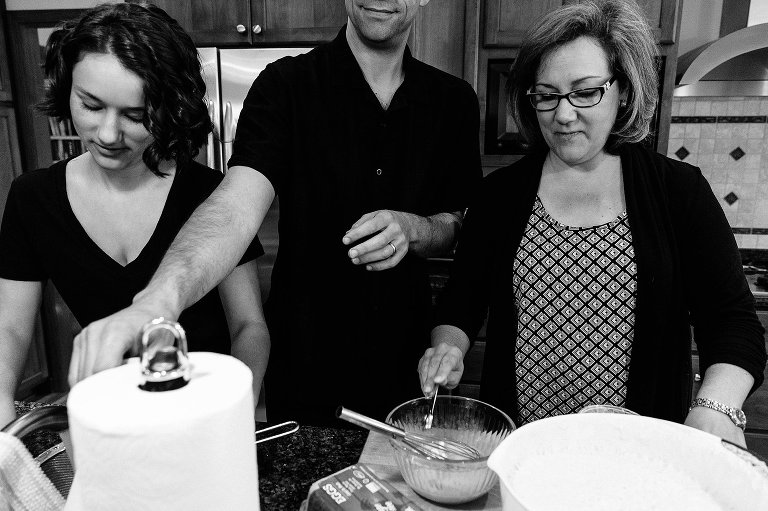 Dad reaches for paper towel between wife and teen daughter preparing breakfast 