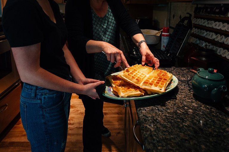 Mom puts hot waffles on a plate that teen daughter is holding. 