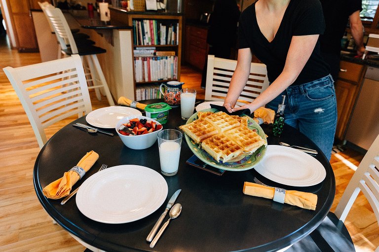 Teen girl puts waffle plate on breakfast table. 