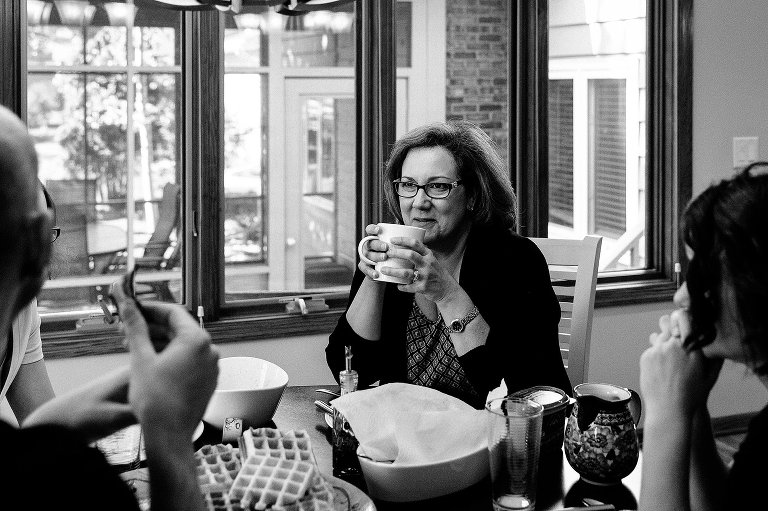 Mom holds coffee cup and listens to family talking at breakfast. 