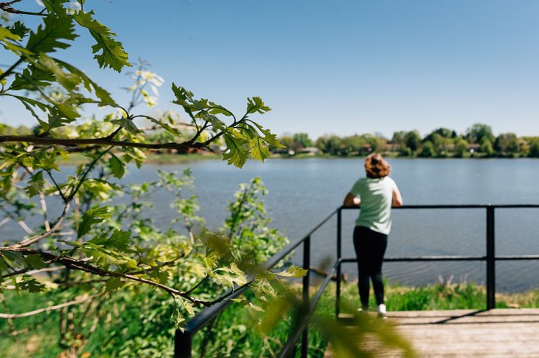 Focus on newly unfurled leaf, indicating spring has arrived. Teen daughter looks out over pond in the distance. 