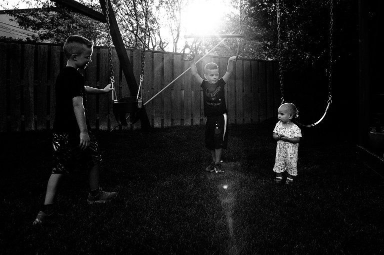 Two boys and toddler girl stand in evening light in backyard