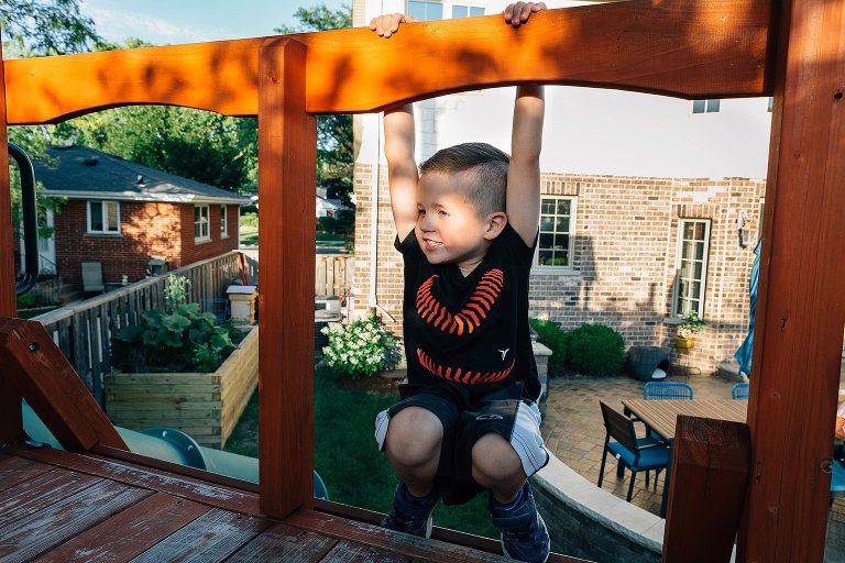 Young boy hangs on backyard play structure 