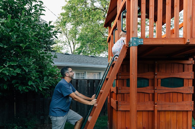 Father stands at bottom of ladder watching toddler climb.