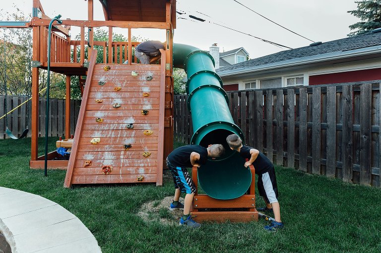 Two brother wait for toddler sister to come down slide. Father at the top of the slide. 