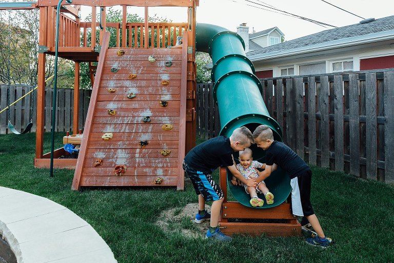 Toddler sister arrives at bottom of the slide. Older brothers catch her. 