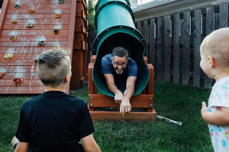 Dad comes down the slide head first, while two kids are waiting for him.