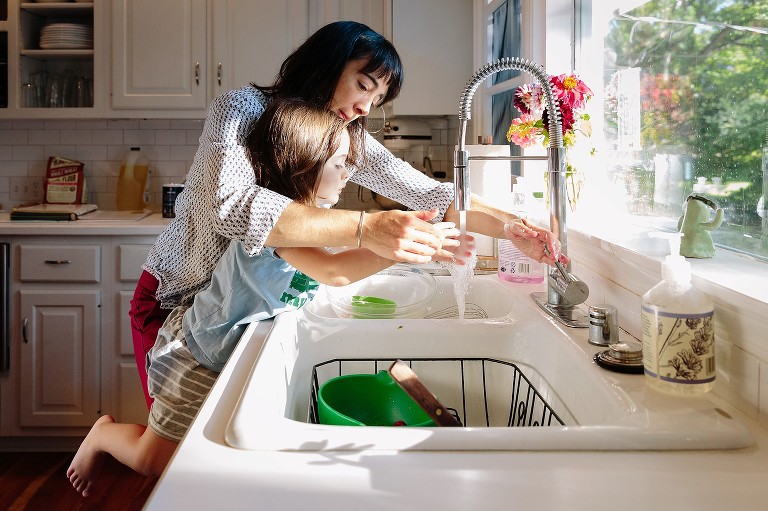 Mother helps daughter wash her hands in the kitchen window 