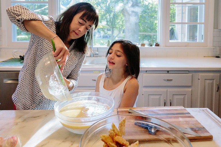 Mom and daughter pour cake batter in large glass bowl.
