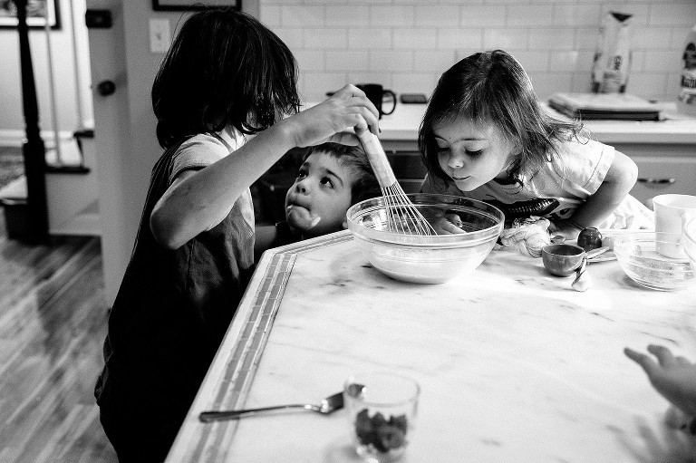 Older bother talks to younger brother while youngest sister examines the whisked eggs 