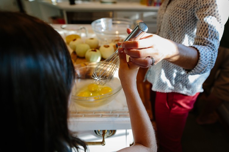 Mom hands child a whisk to whisk eggs for batter