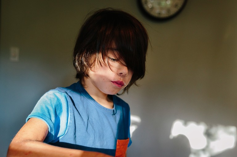 Older boy sits in dappled light in kitchen 