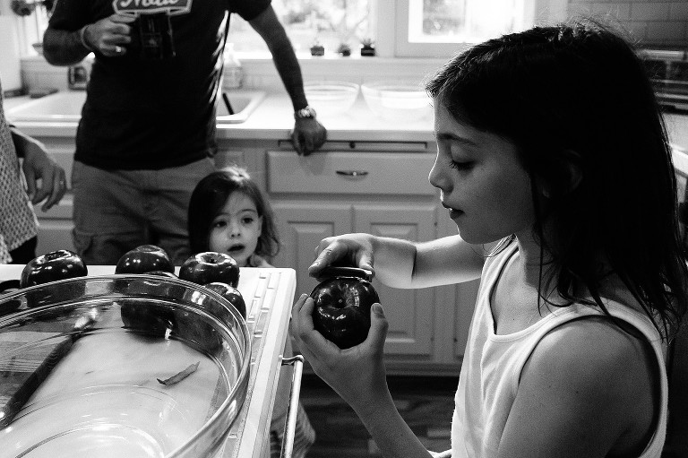 Older sister peels apples, while younger sister and dad with coffee look on