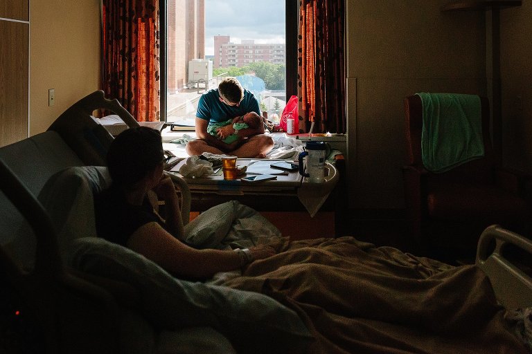Dad sits in the window after newborn is born. Mom watches from from hospital bed. 