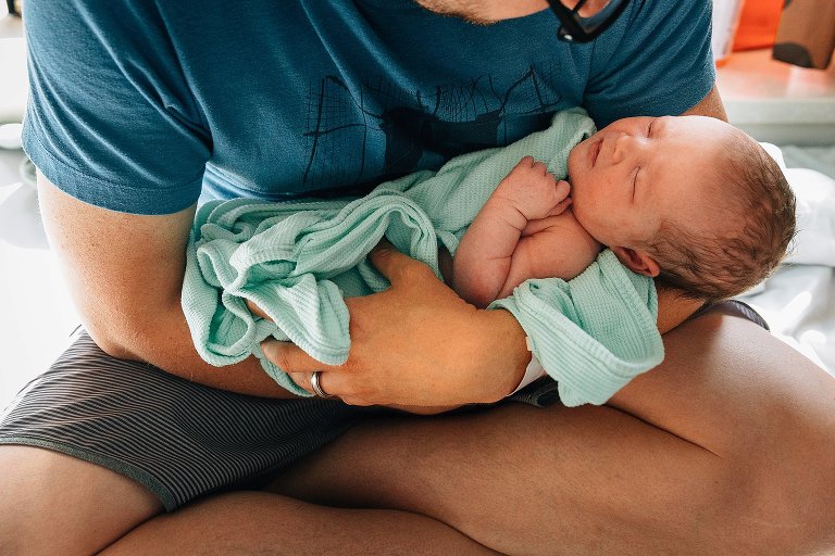 Dad holds newborn in hospital window light 