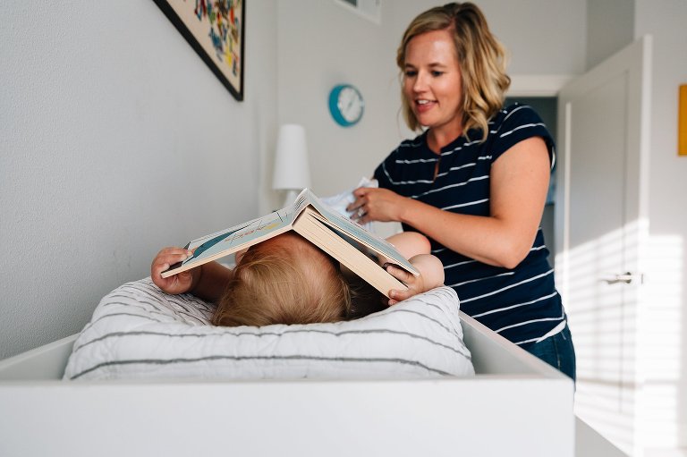 toddler lays a heavy board book on his face while mom gets him dressed for bed 