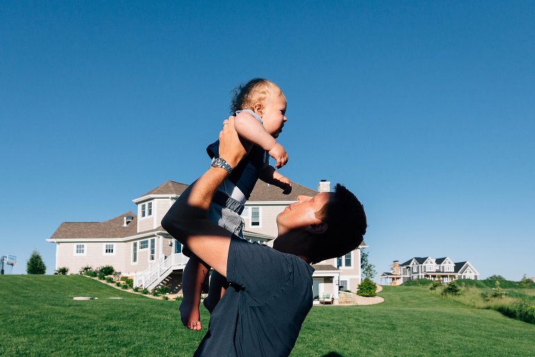 dad holds up toddler son in backyard