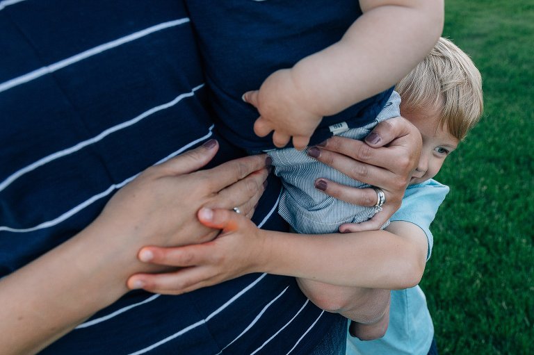 Mom holds toddler son while preschool son gives both a big hug