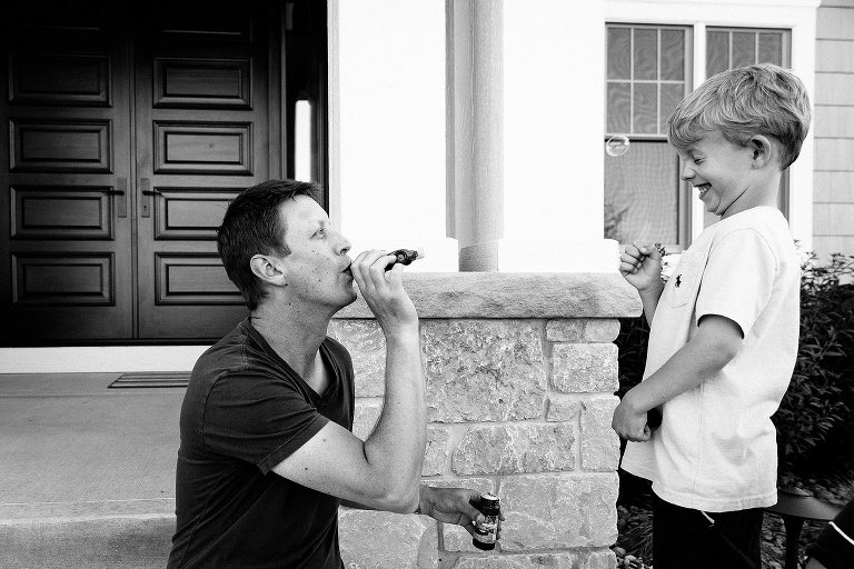 Dad and preschool son blow bubbles in front of family home