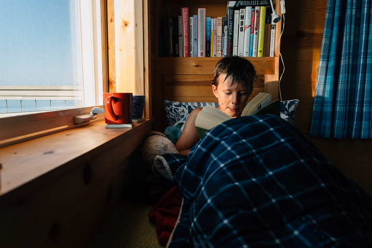 Boy reads book in lake house window
