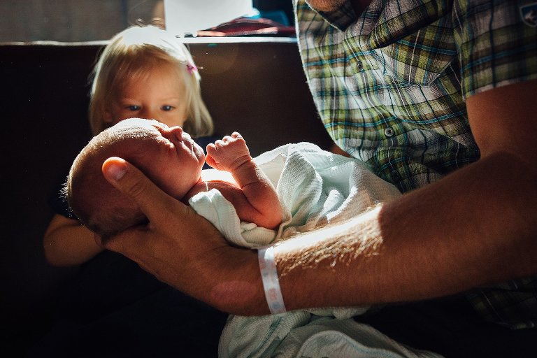 Dad holds newborn while big sister looks on
