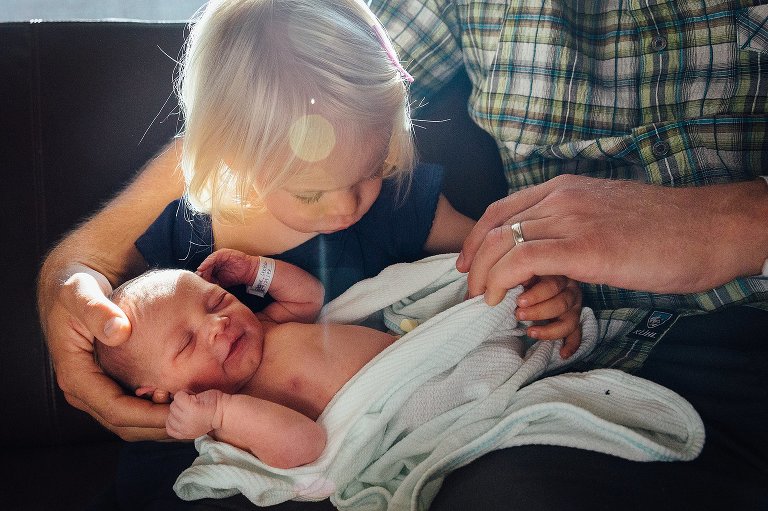 big sister holds newborn sibling and checks for belly button 