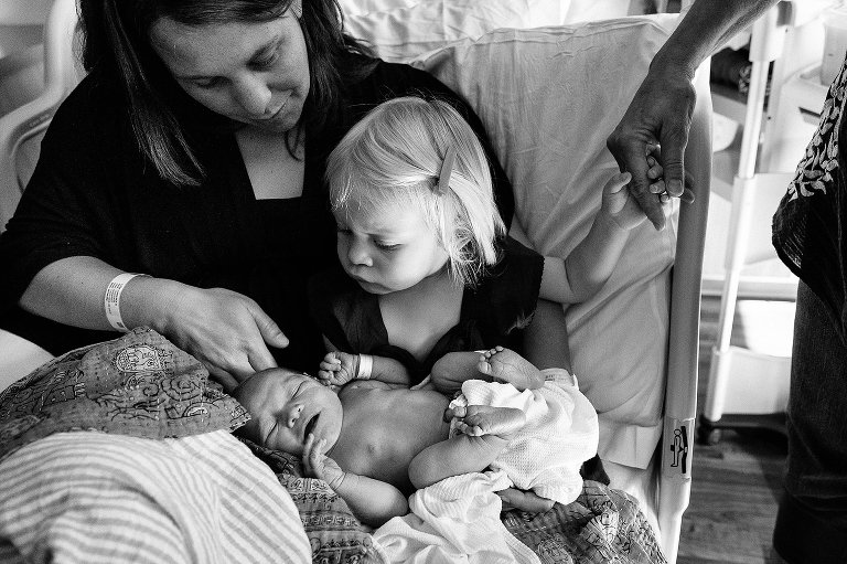 Toddler holds grandma's hand while sitting with mom and meeting new sister