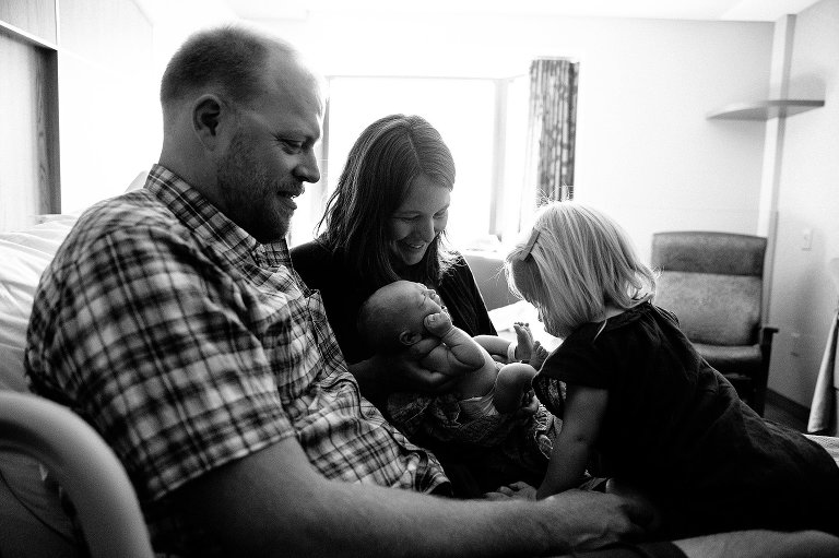 newborn yawns while big sister examines toes