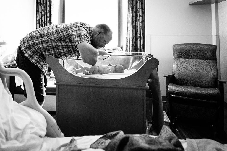 Dad looks at newborn in hospital basinet 