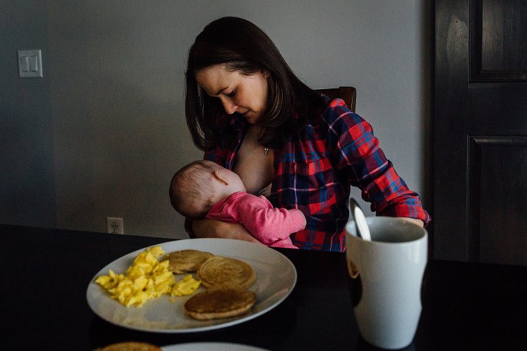 Mom concentrate on nursing baby while full plate of hot breakfast sits untouched 