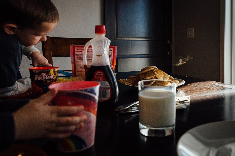 Boy and girl sit at breakfast table. Steam rising off mountain of pancakes. 