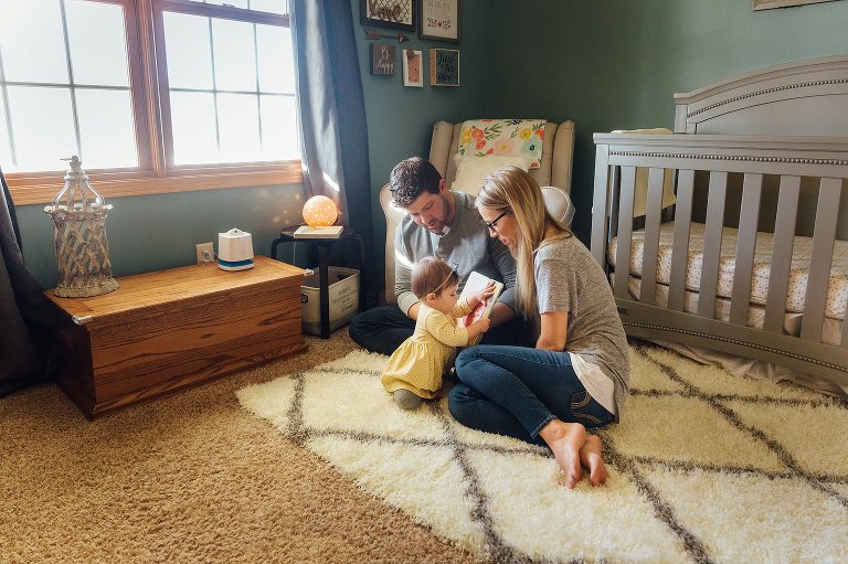 A young family reads a book in the nursery together.