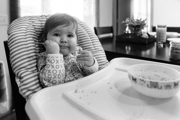 Baby uses spoon to feed self sitting in high chair